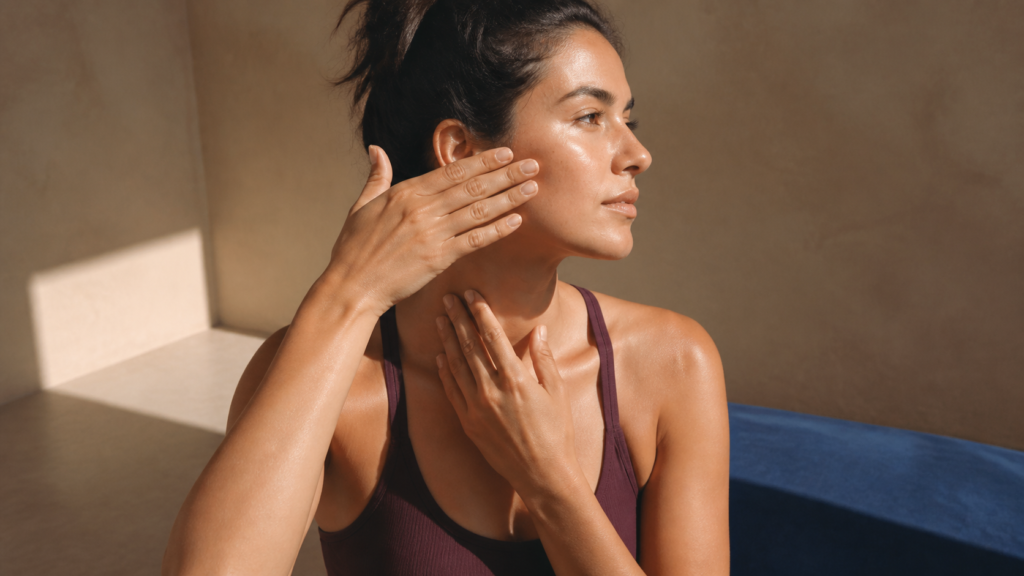 Woman moving gentle facial massage strokes toward her ear and down the side of her neck.